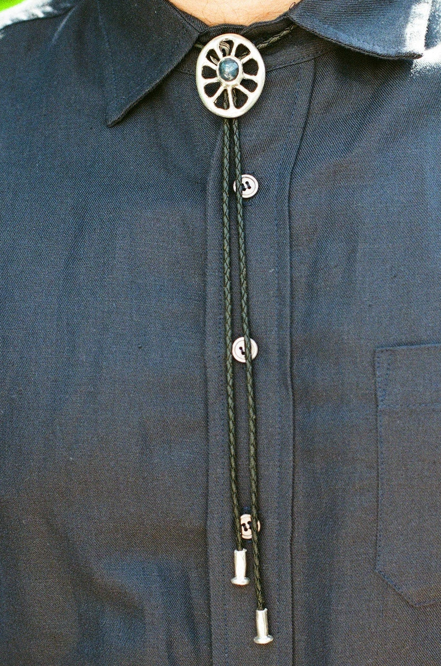 Close-up of a dark shirt with a decorative bolo tie against a blurred natural background