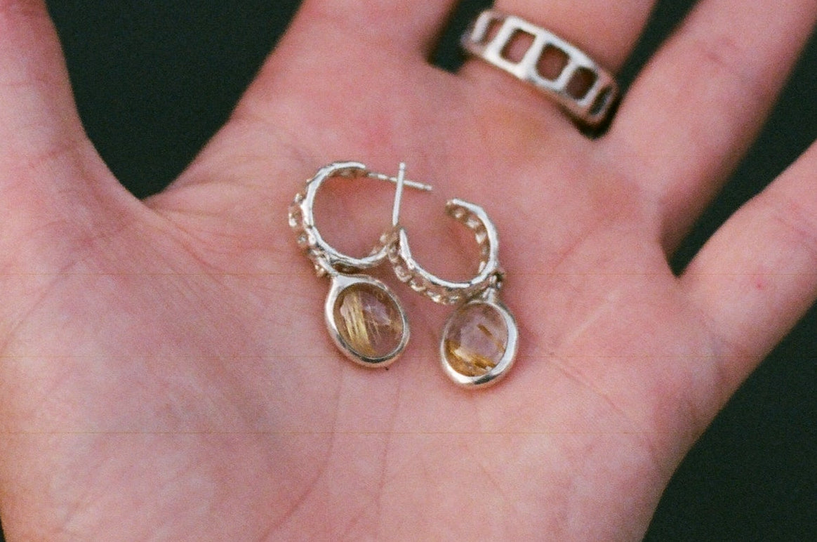 Hand holding a pair of earrings against a dark background