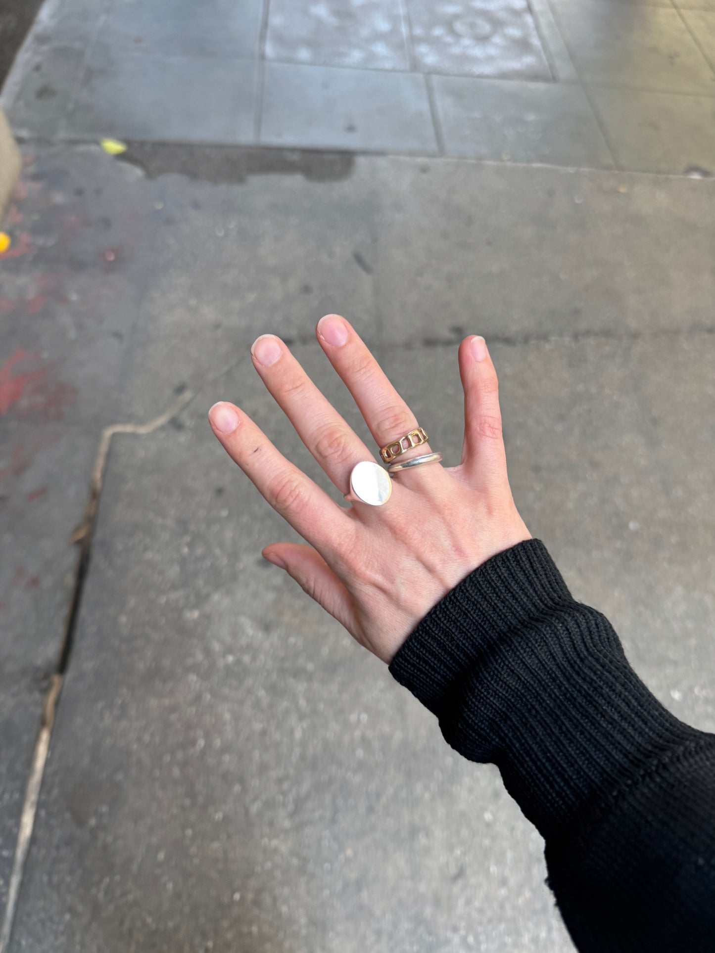 Hand with multiple rings on a gray pavement background
