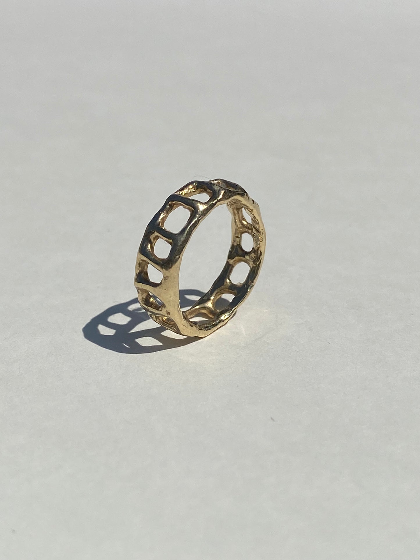 Gold ring with cage-like design on a light gray background