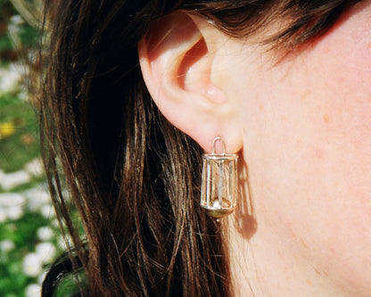 Close-up of a person wearing a silver column like earring swith a blurred natural background