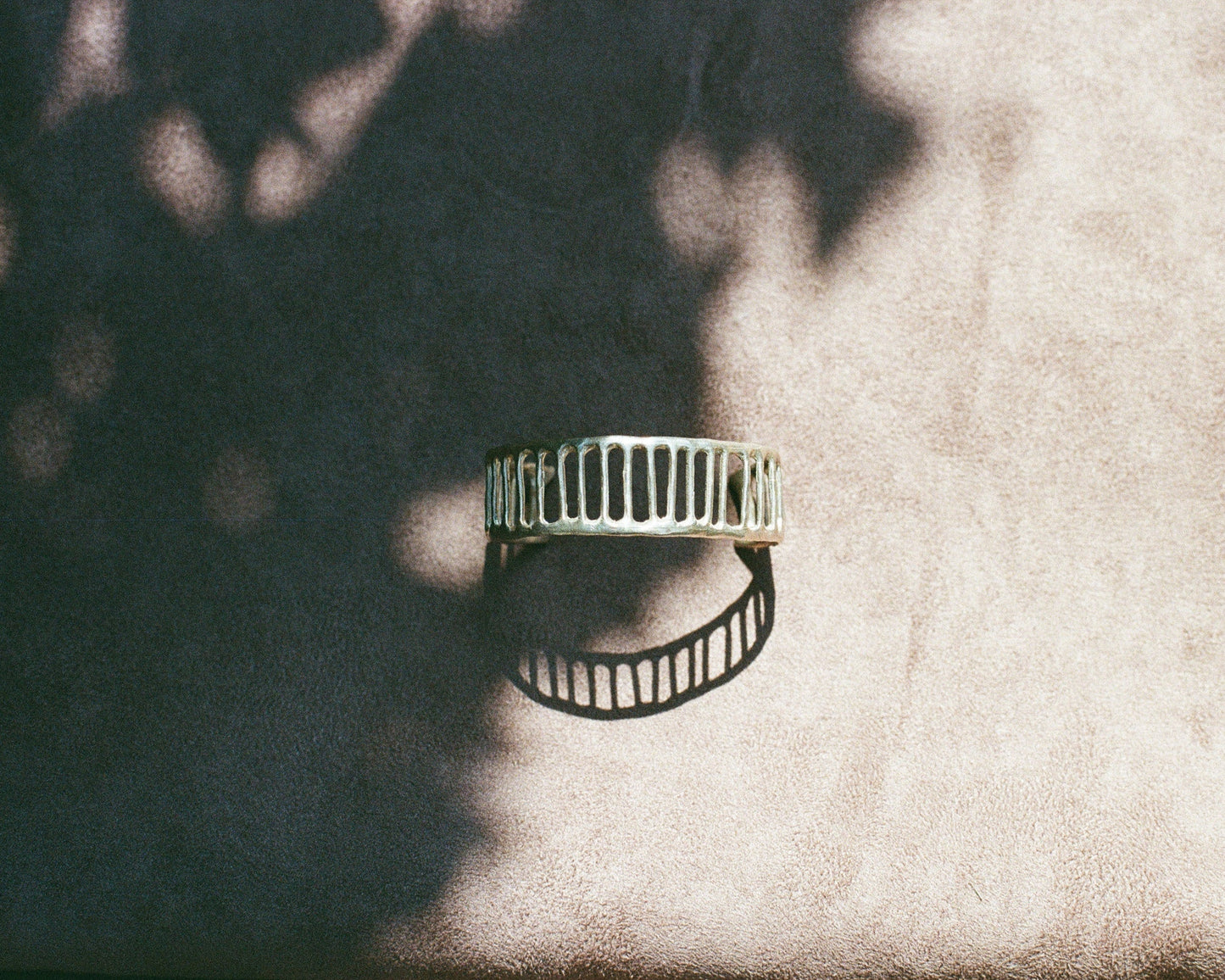 Silver cuff on a textured beige surface with leaf shadows