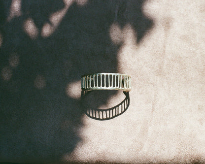 Silver cuff on a textured beige surface with leaf shadows