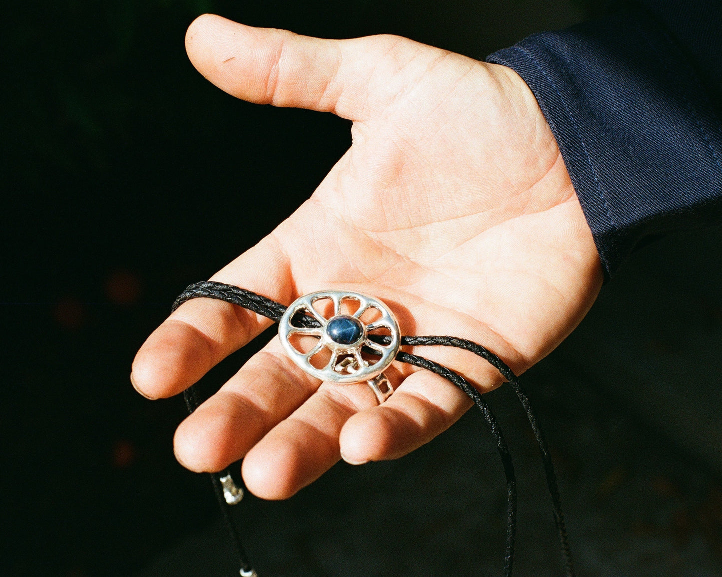 Hand holding a decorative bolo tie with a blue star sapphire against a dark background