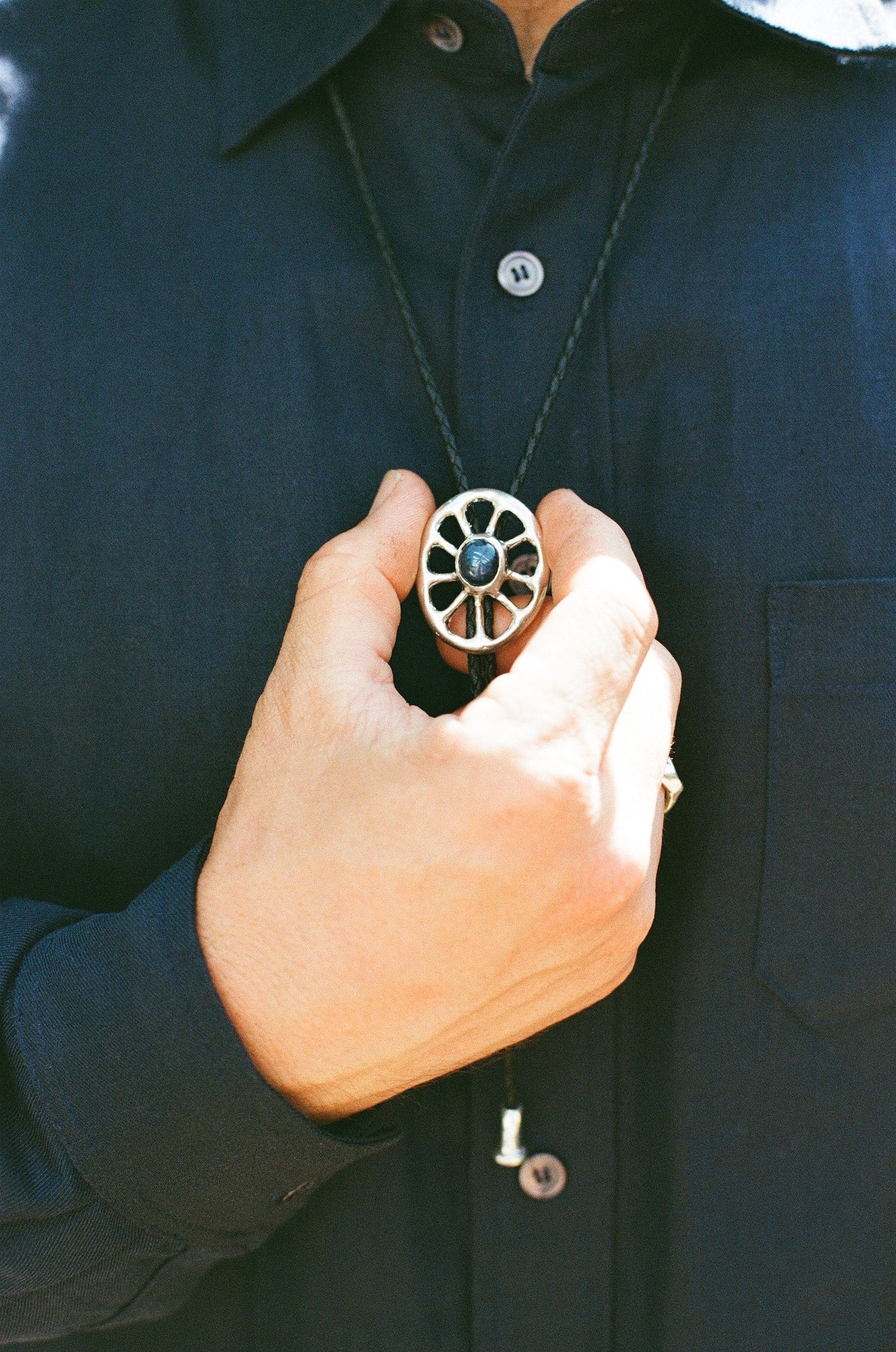 Person holding a unique bolo tie with a inset star sapphire against a dark background