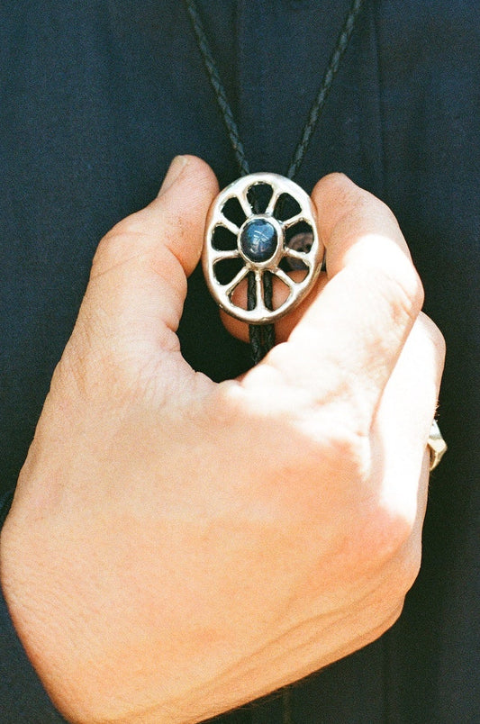 Person holding a unique bolo tie with a inset star sapphire against a dark background