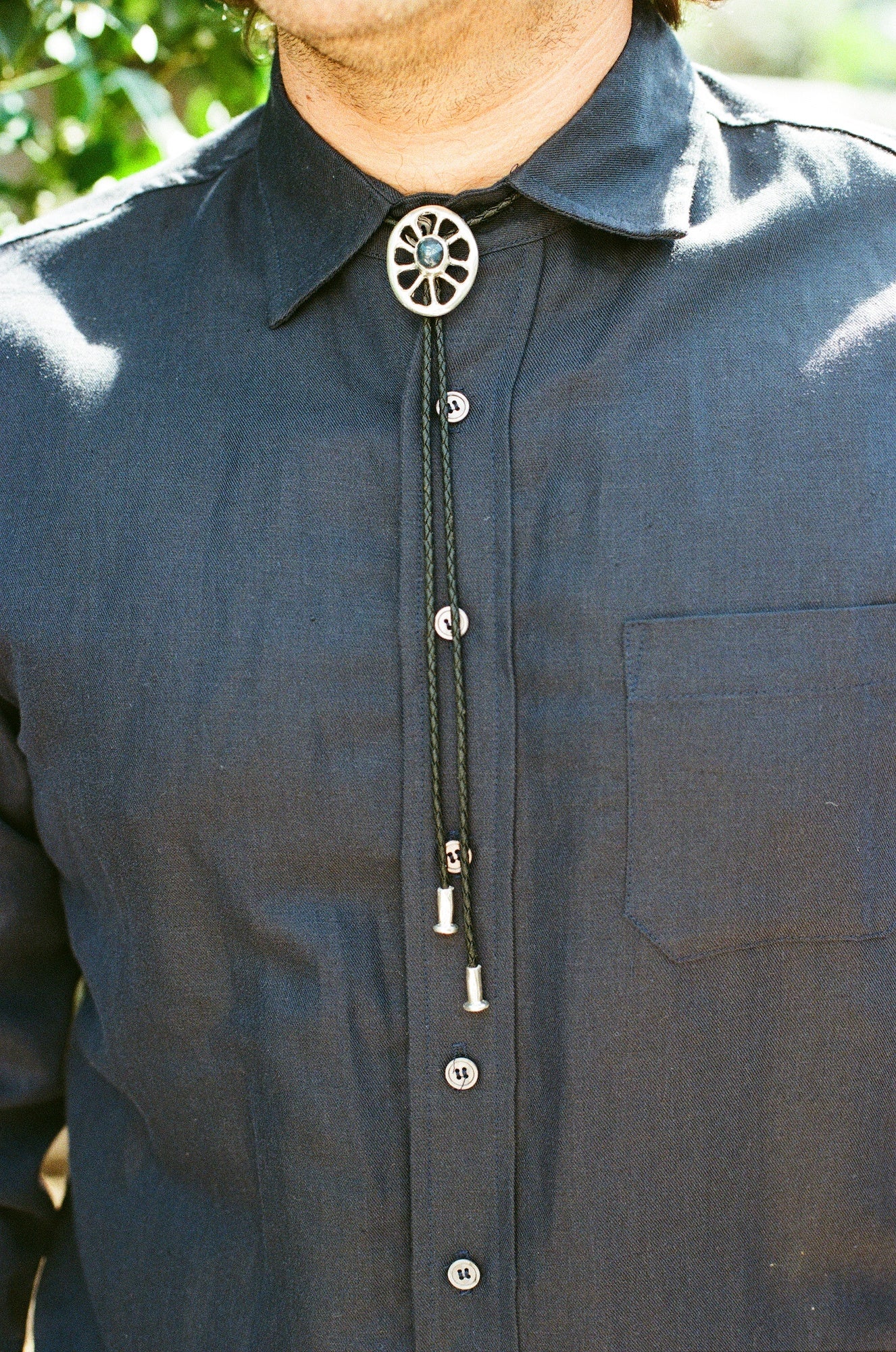Close-up of a dark shirt with a decorative bolo tie against a blurred natural background