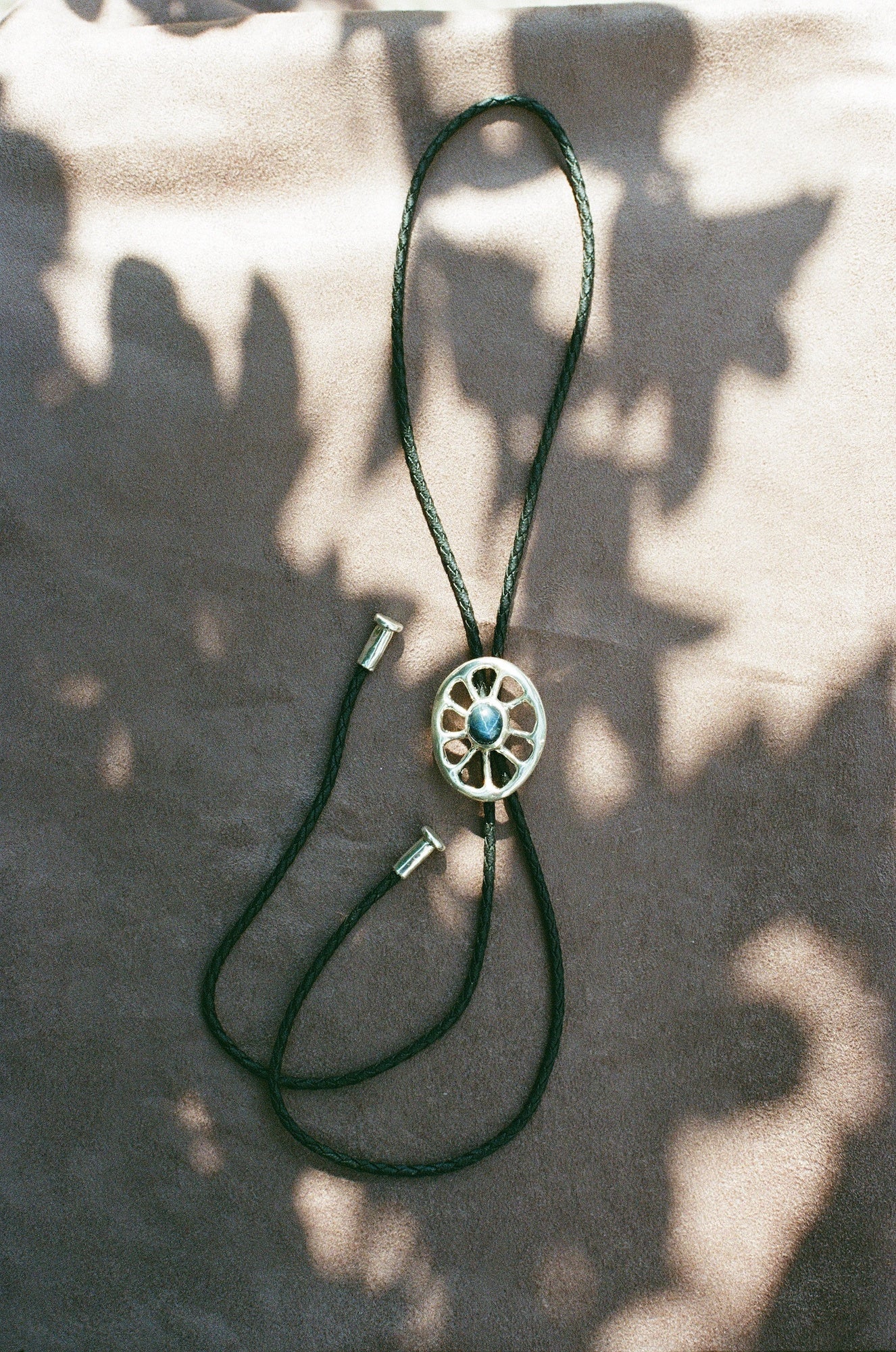 Black leather bolo tie with a silver and blue star sapphire center on a textured surface