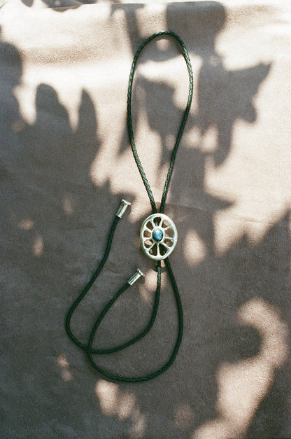 Black leather bolo tie with a silver and blue star sapphire center on a textured surface