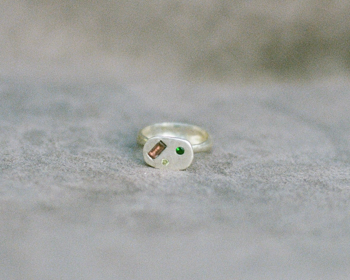Silver ring with embedded gemstones on a textured gray surface