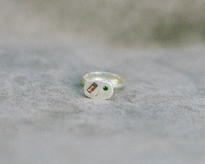 Silver ring with embedded gemstones on a textured gray surface