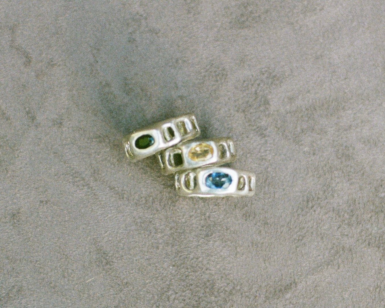 Three silver rings with embedded gemstones on a textured surface
