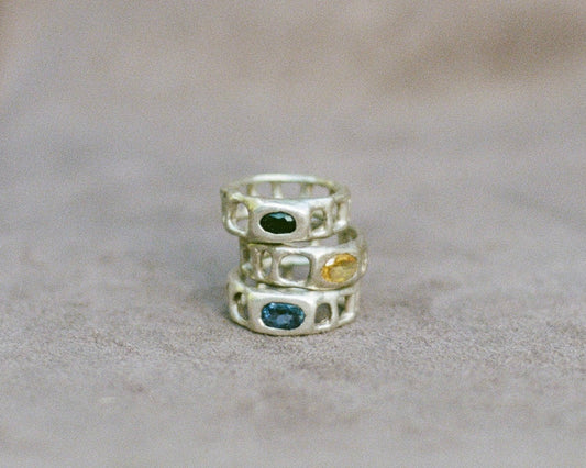 Three silver rings with embedded gemstones on a beige surface
