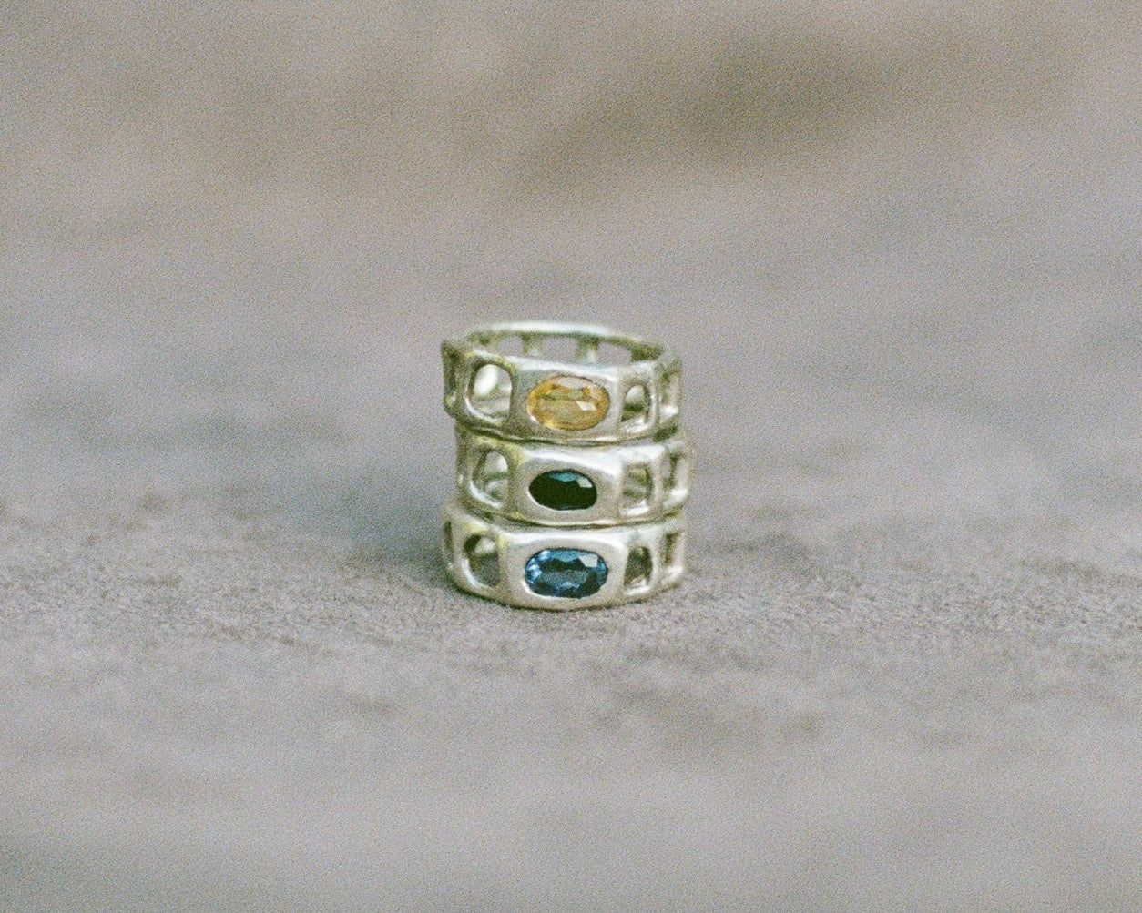 Stack of three silver rings with embedded gemstones on a beige surface