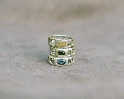 Stack of three silver rings with embedded gemstones on a beige surface