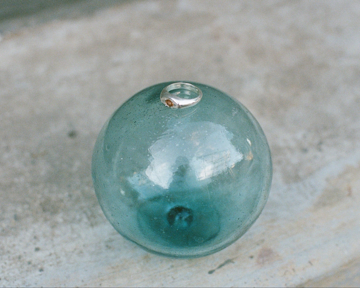 Teal glass sphere with a silver ring on a concrete surface