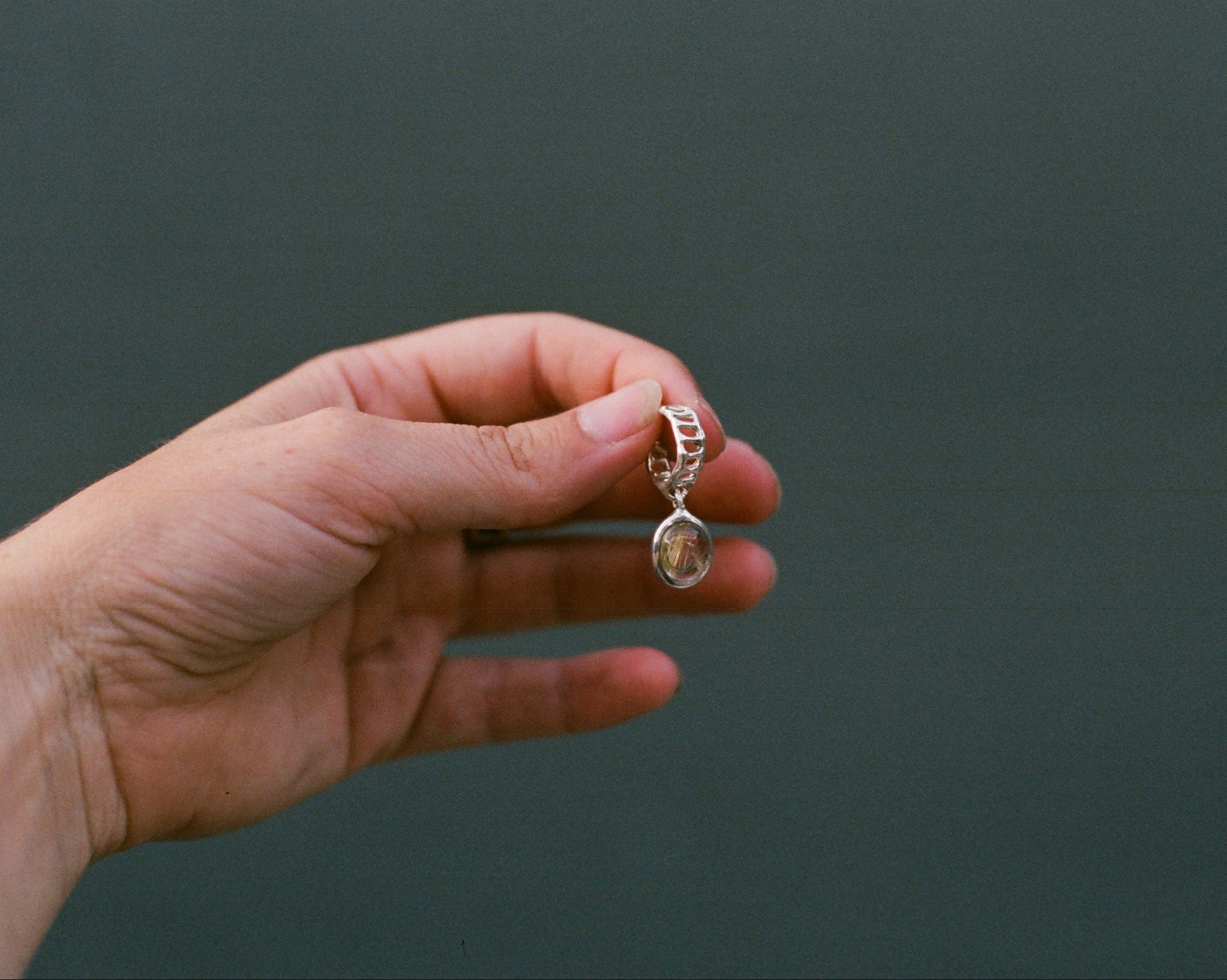 Hand holding a silver teardrop-shaped earring against a dark background