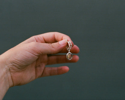 Hand holding a silver teardrop-shaped earring against a dark background