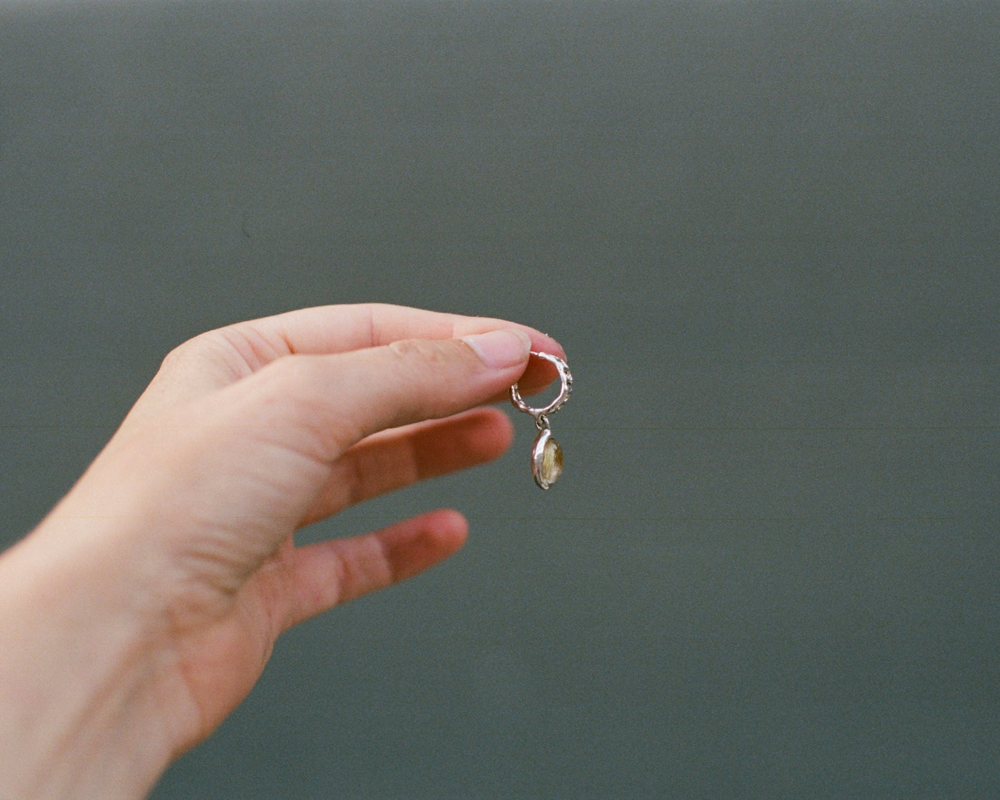 Hand holding a small earring against a plain background