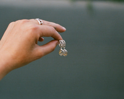 Hand holding a silver earrings with a rutilated quartz gemstone against a blurred green background