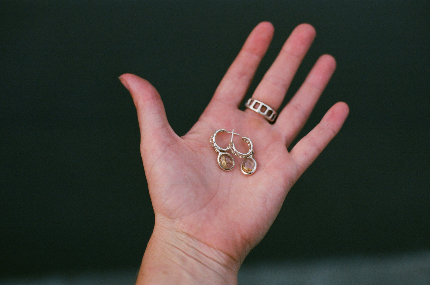 Hand holding a pair of earrings against a dark background