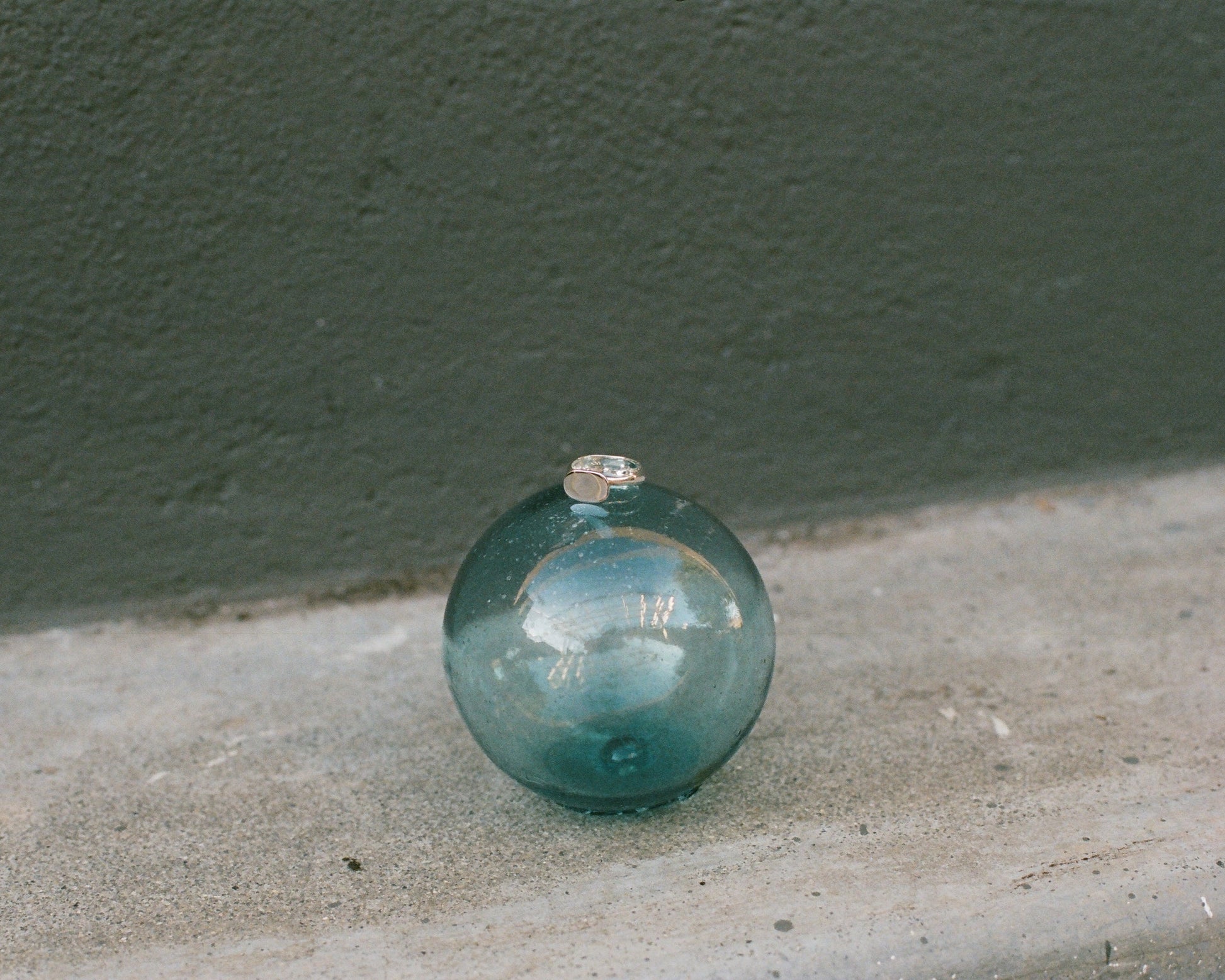 Silver ring on a green glass sphere on a concrete surface with a dark green wall in the background