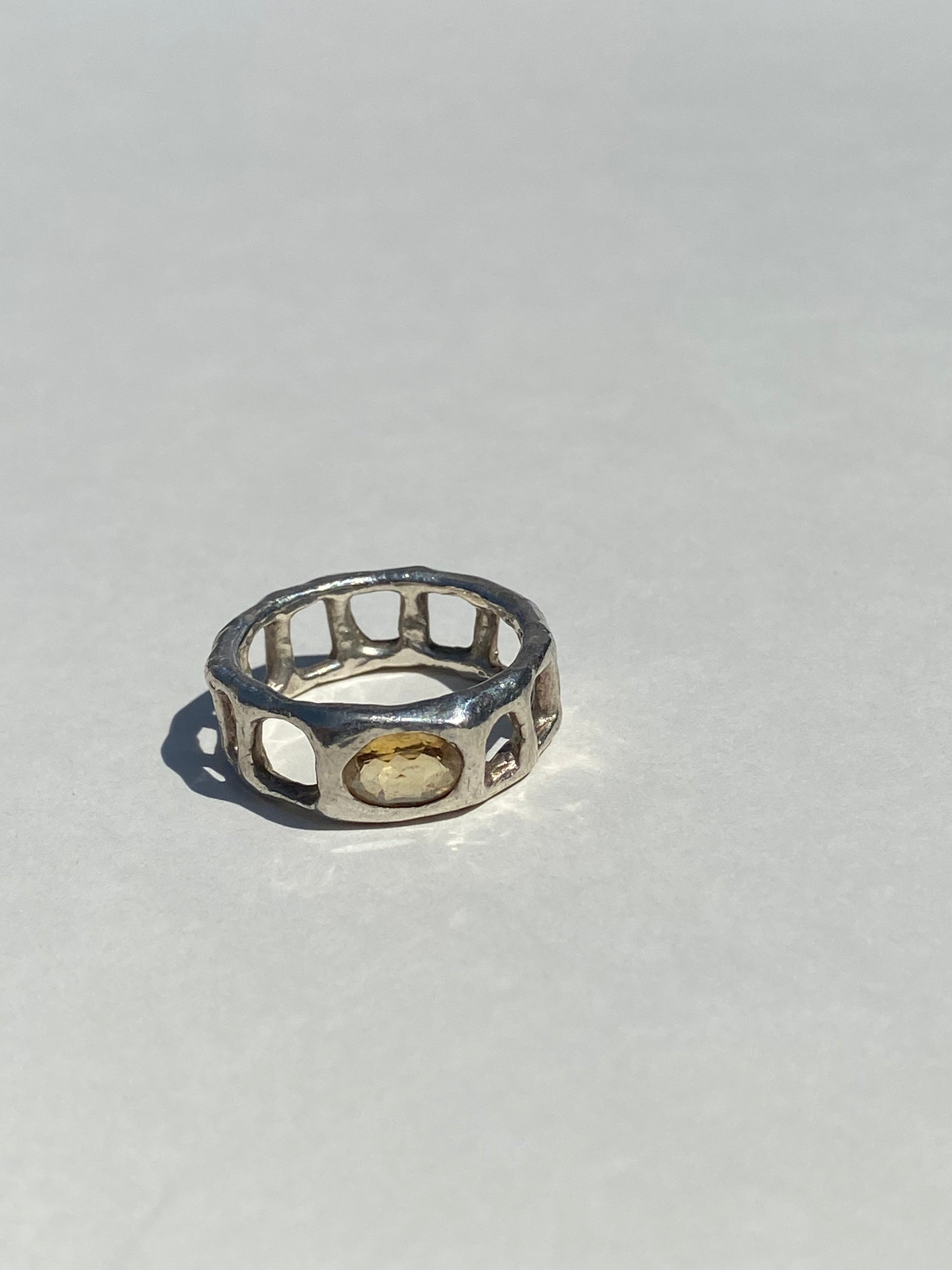 Silver ring with a yellow gemstone on a light gray background