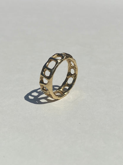 Gold ring with cage-like design on a light gray background