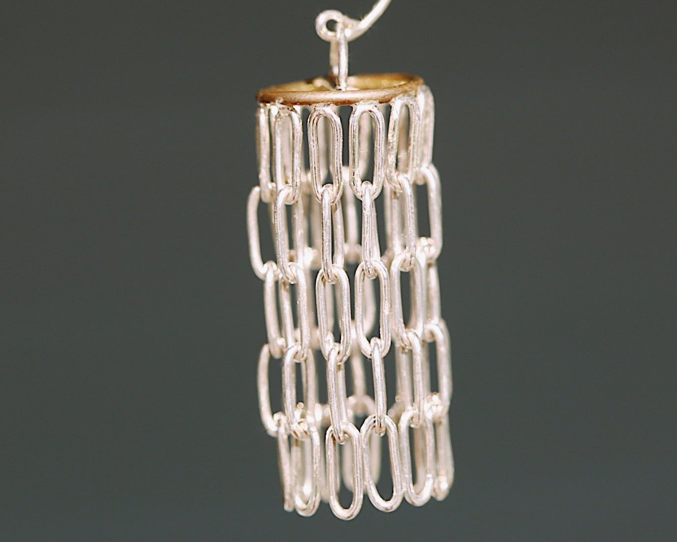 Silver and gold chandelier like earrings against a blurred grey background