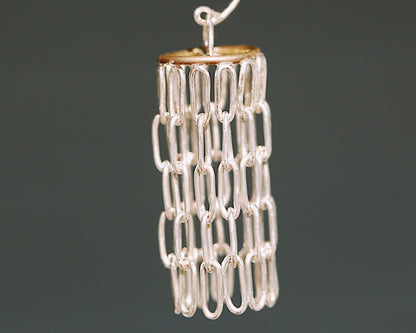 Silver and gold chandelier like earrings against a blurred grey background