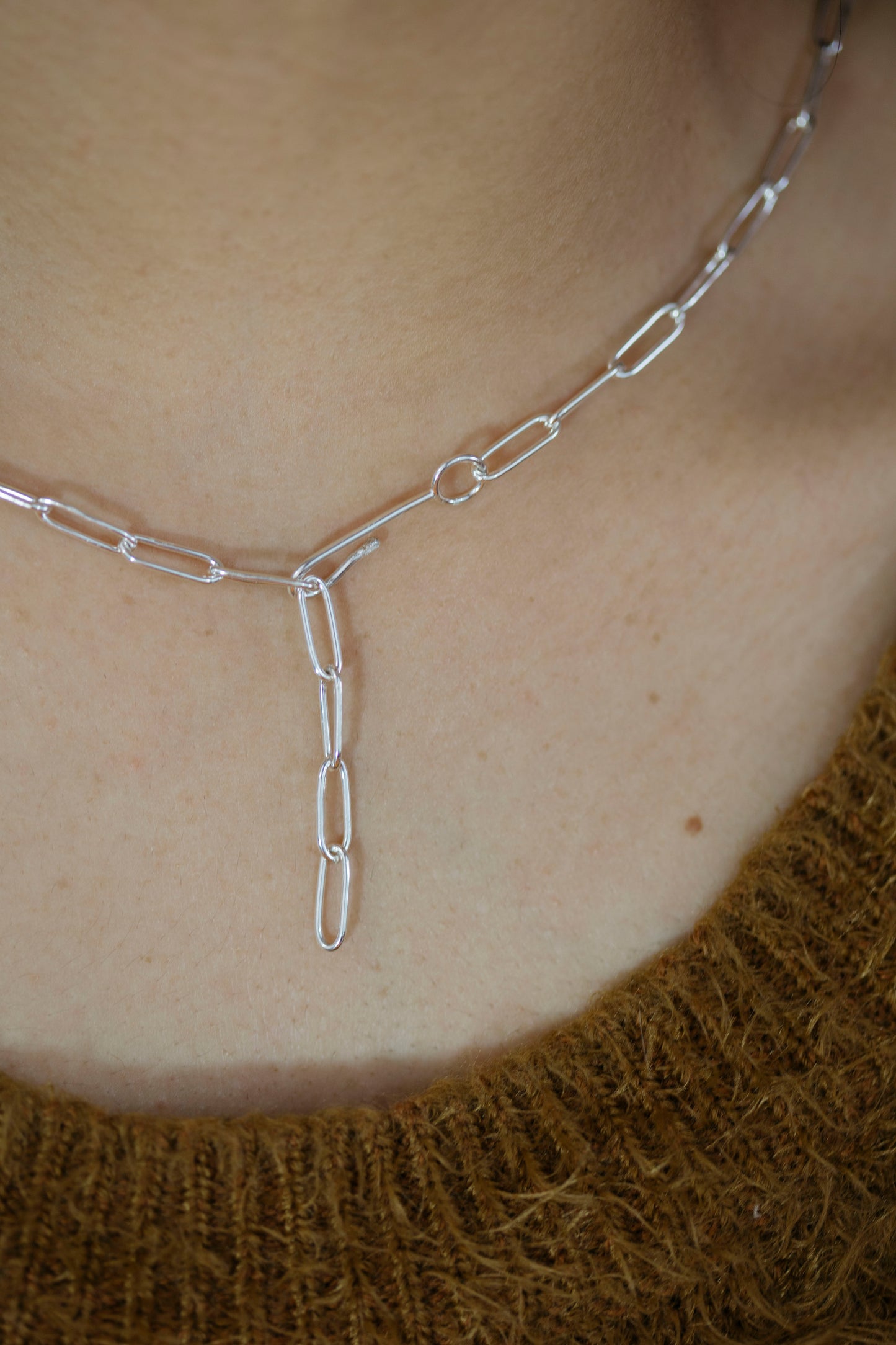 Silver chain necklace on a person's neck with a blurred background
