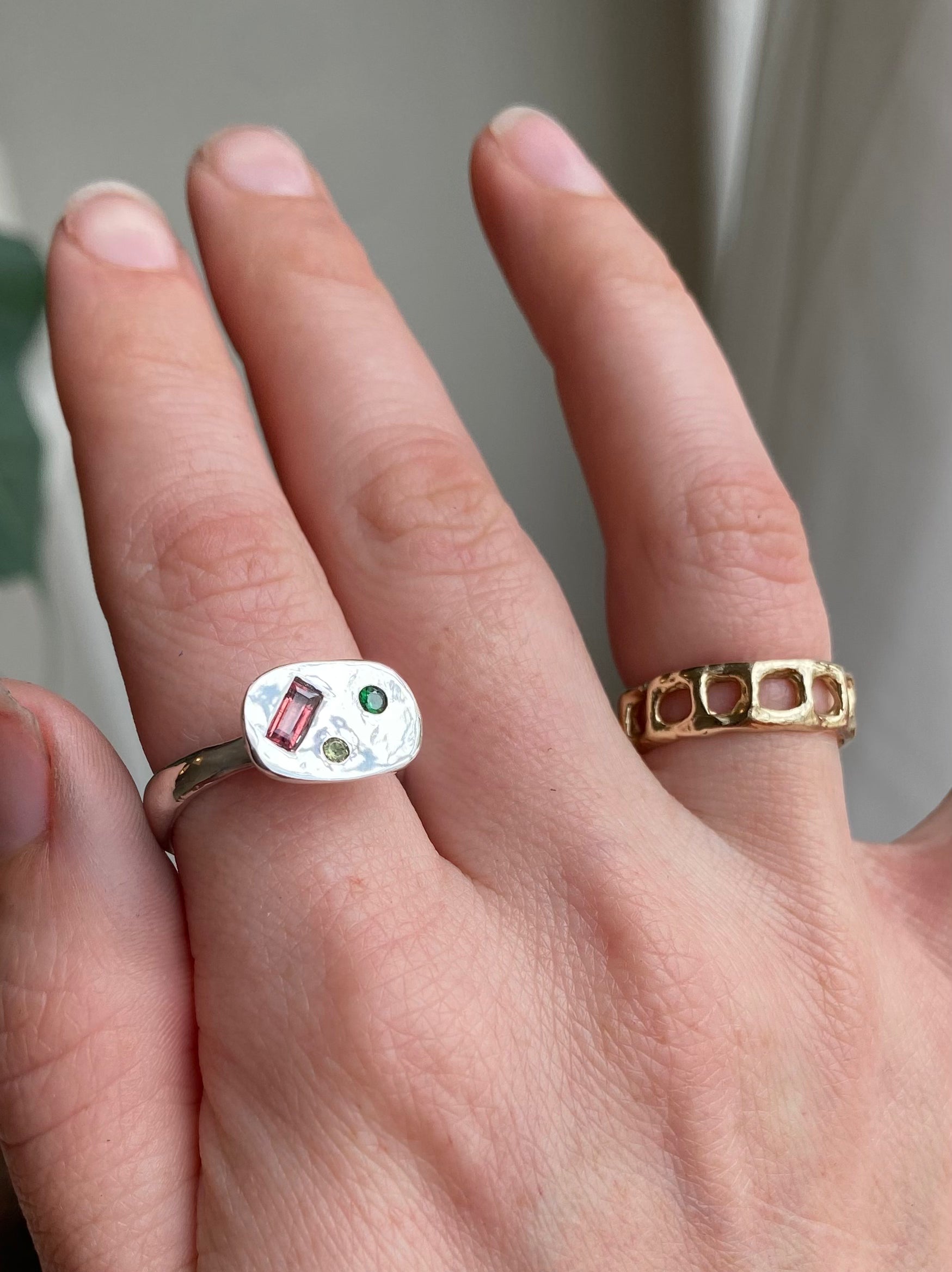 Hand wearing two rings with gemstones on a neutral background