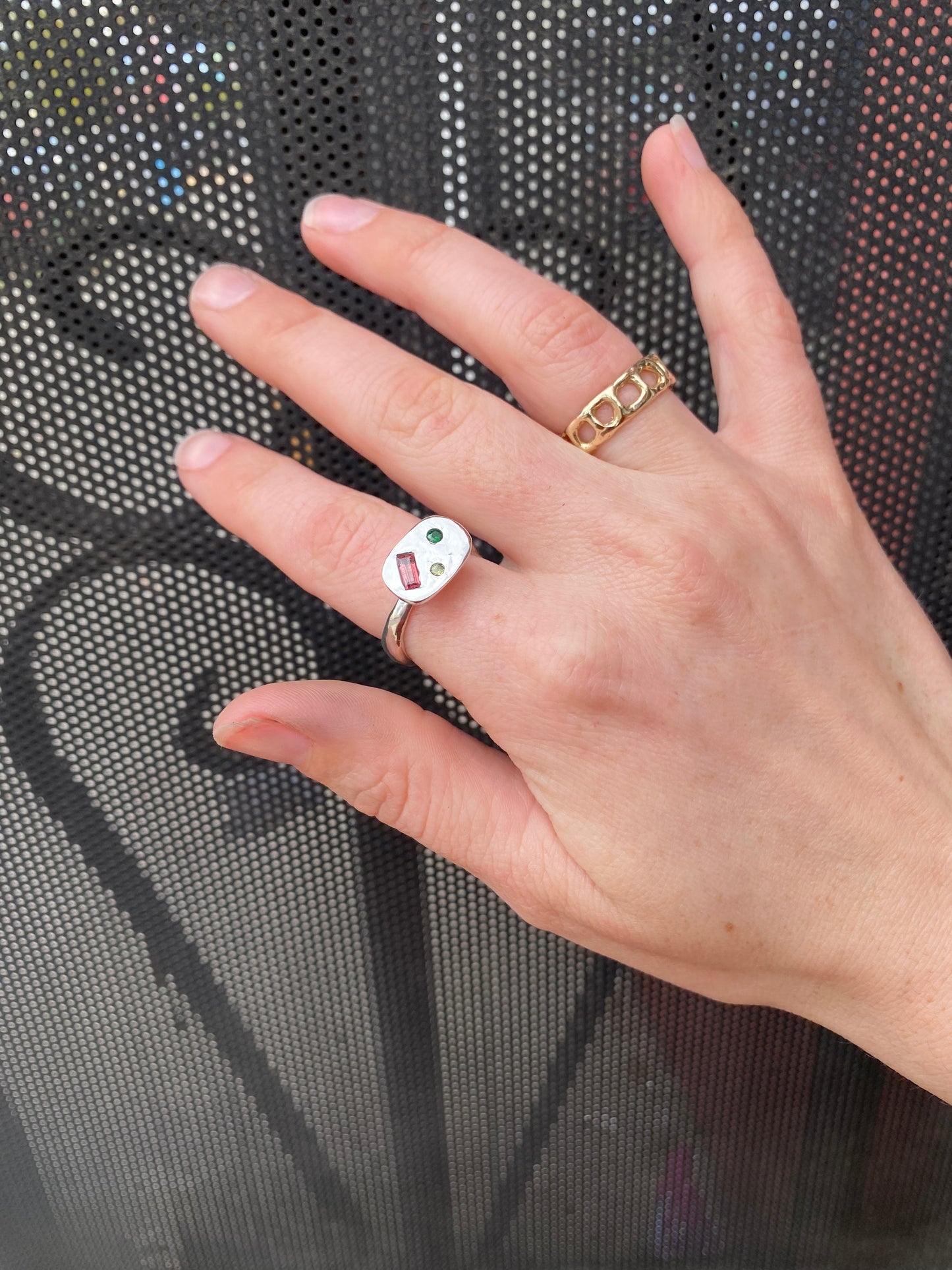 Hand wearing a silver ring with gemstones against a textured black background