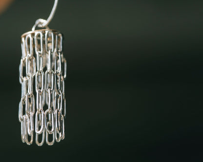 Silver and gold chandelier like earrings against a blurred grey background
